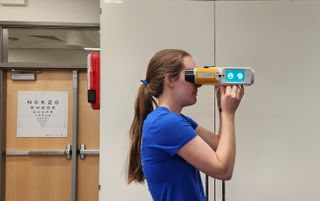 a person holds a binocular-like device up to their eyes in a laboratory