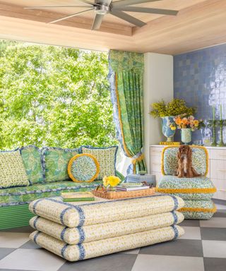 outdoor living room with checkerboard patio tile and a set of floral william morris printed sofa, ottoman, and armchair with a small dog