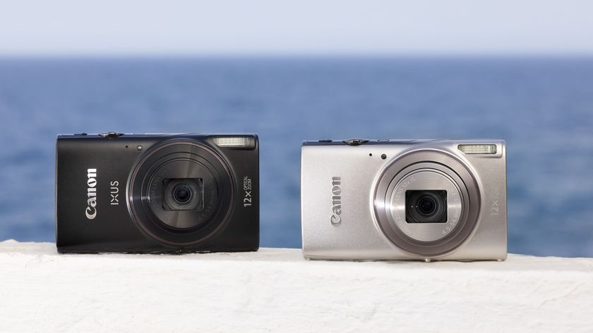 Canon PowerShot Ixus 285 HS A point and shoot camera in black and in silver on a white wall by the ocean on a sunny day