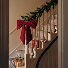 A staircase decorated with a Christmas garland and an extra large red velvet Christmas bow