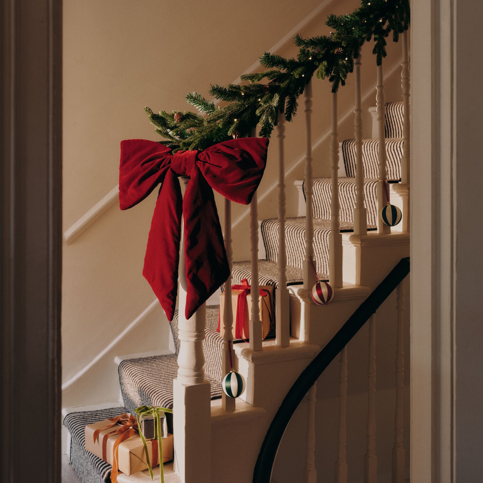 A staircase decorated with a Christmas garland and an extra large red velvet Christmas bow