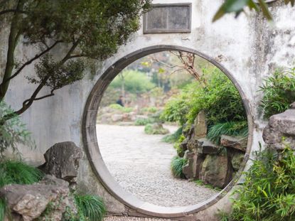 A stone wall with a circular opening in a garden