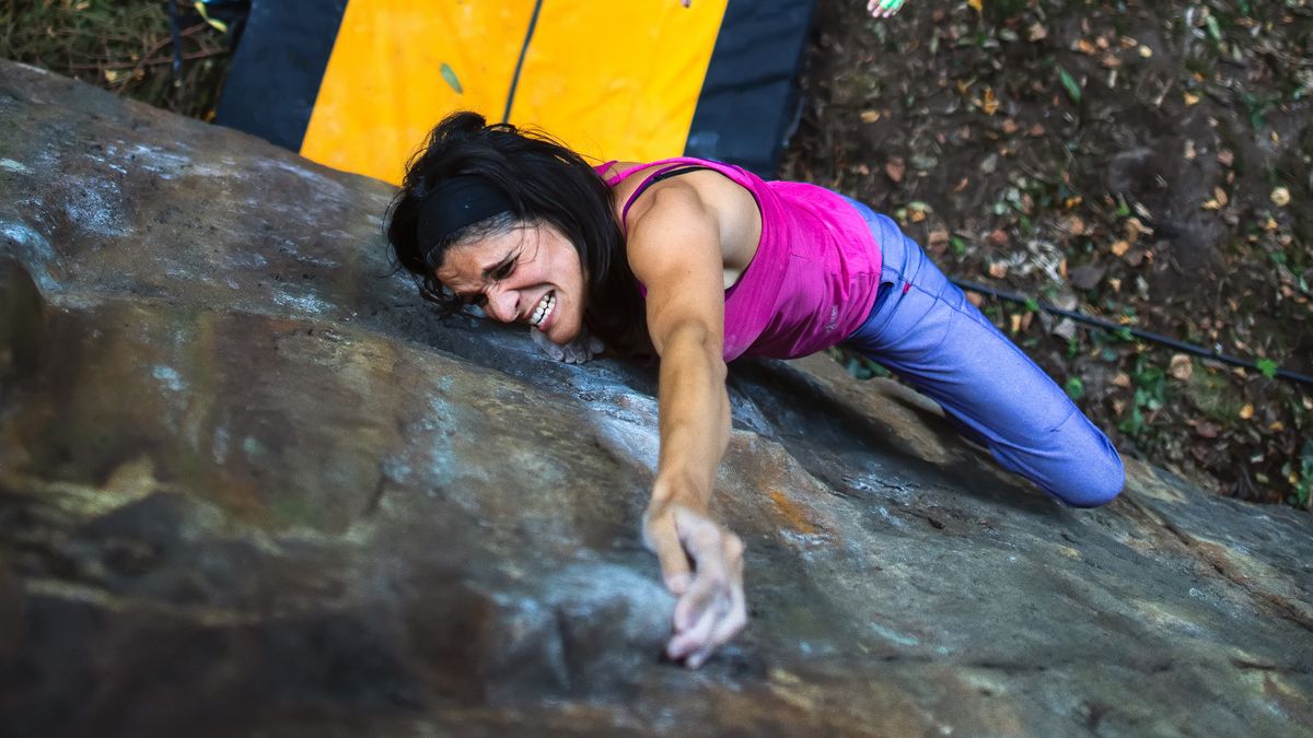 A woman bouldering above a yellow crash pad