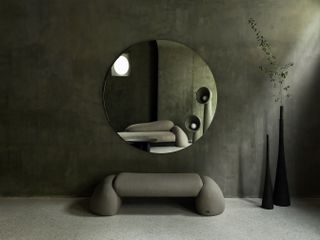 A large round mirror hangs on the wall over an upholstered bench by Faina