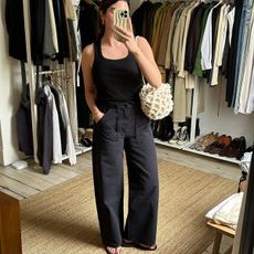 Influencer Anna Newton wears a pair of black jeans and black scoop neck top with black flip flops. 