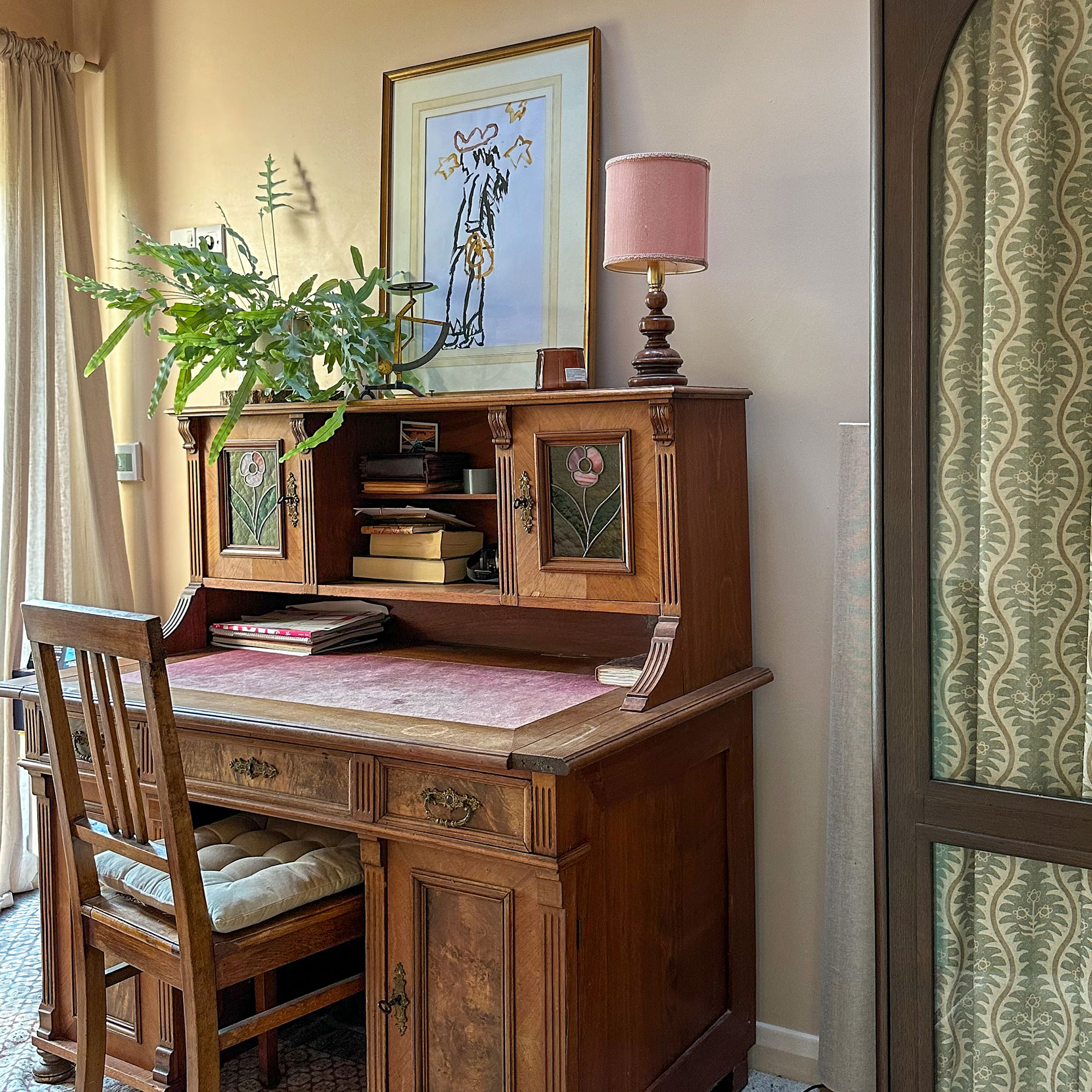 Antique wooden desk with wooden chair, beside wardrobe with glass doors showing patterned fabric behind