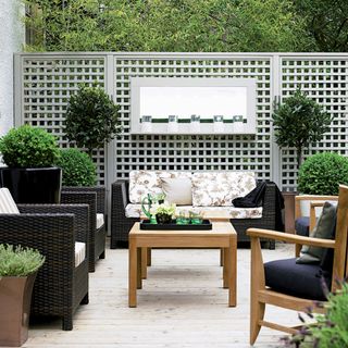 garden area with garden trellis and sofa with cushions and coffee table with plants and shrubs