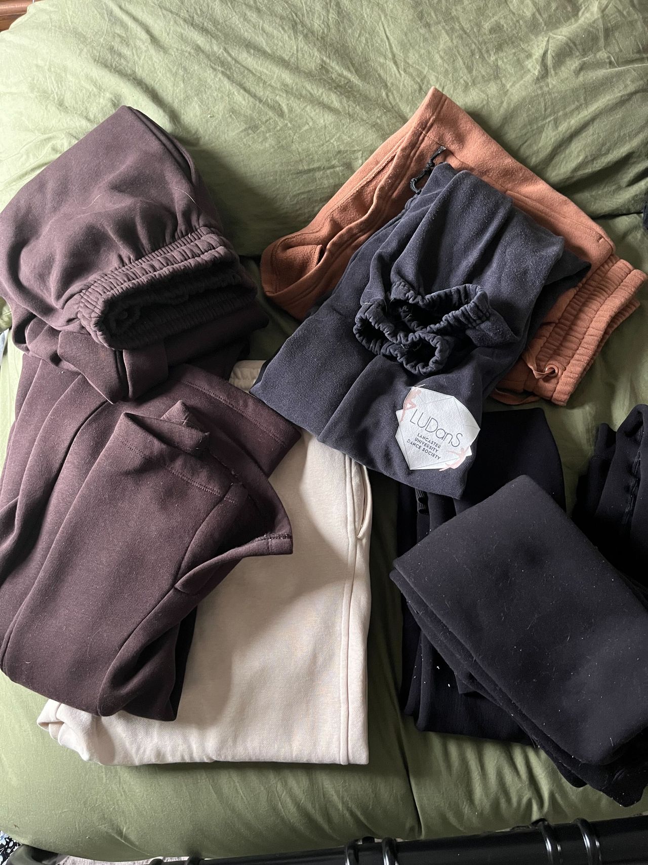 A pile of half folded sweatpants on a green bed