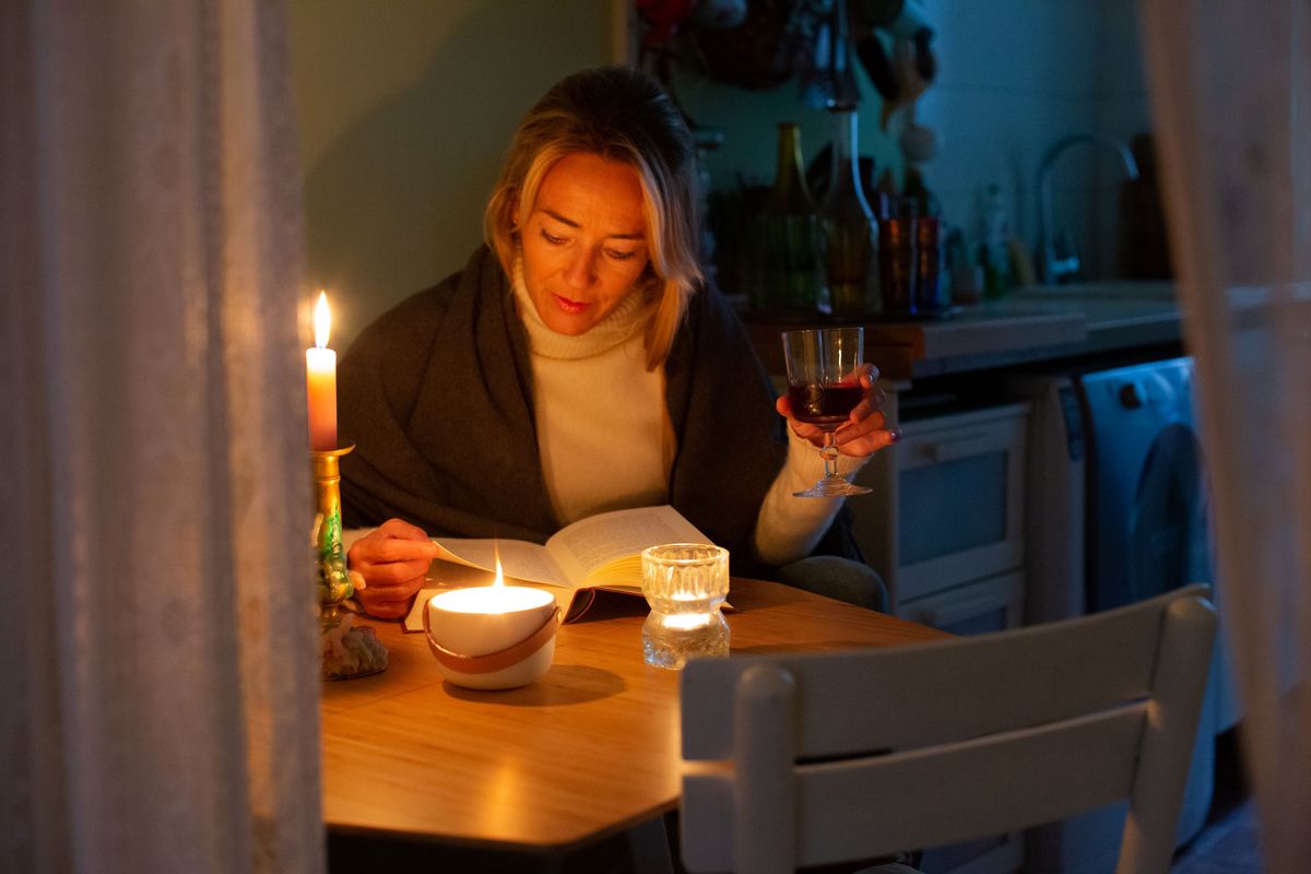 A woman drinking a glass of red win at a kitchen table by candlelight with all the electrics turned off