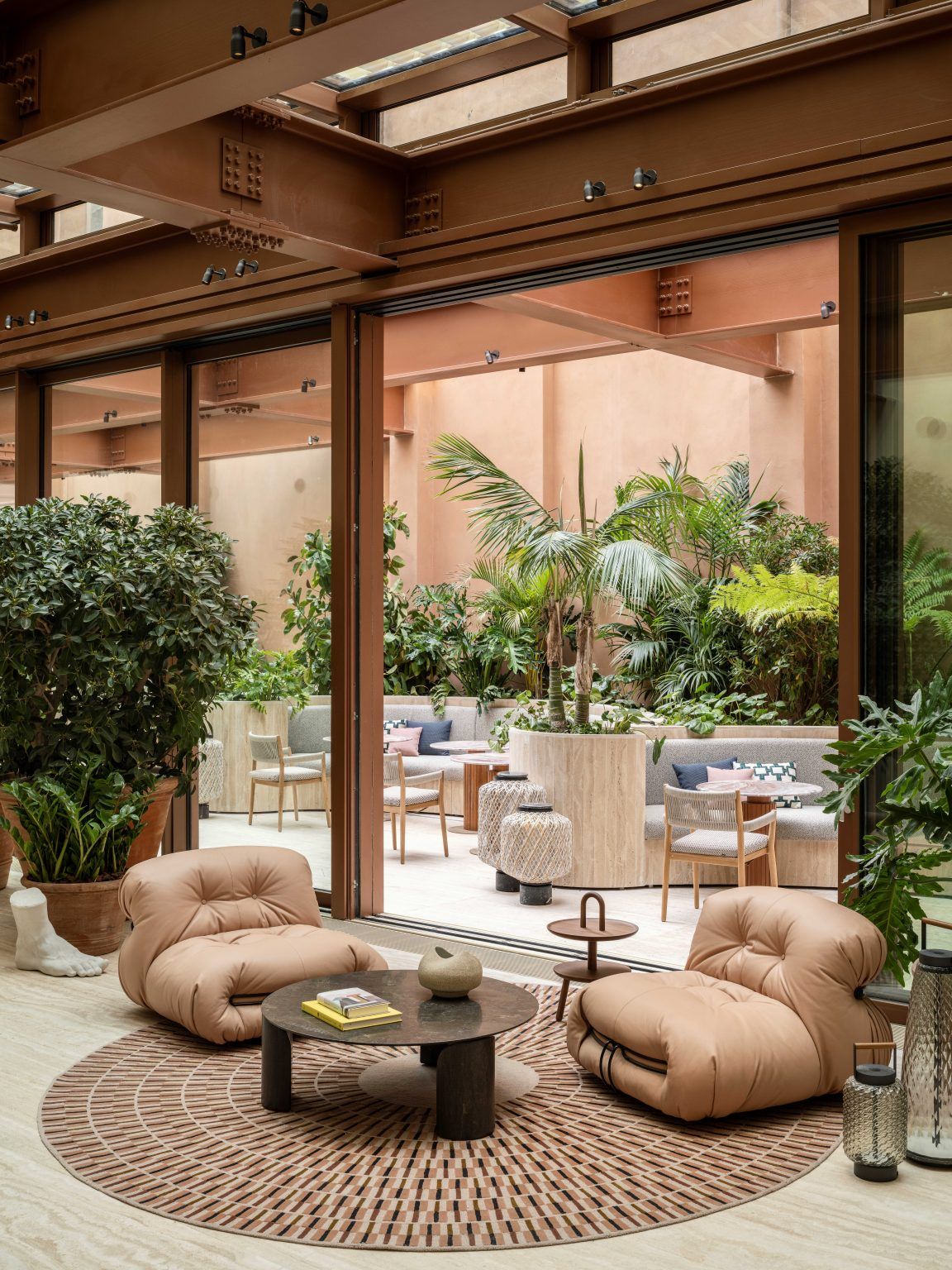 A beautifully furnished and decorated hotel patio bar features soft upholstered leather furniture, round-shaped additions, and plenty of plants.
