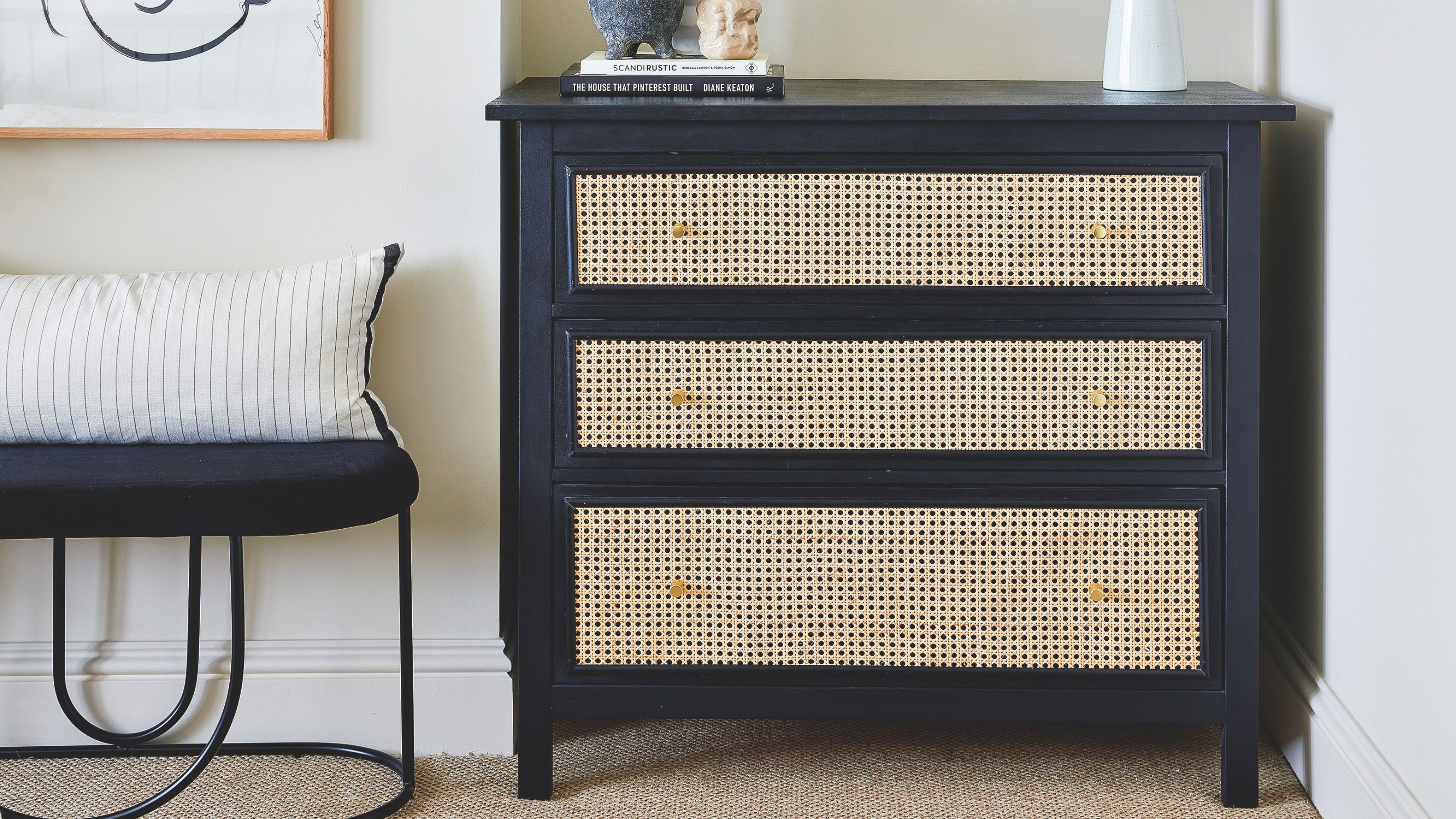 Beige painted bedroom with a black chest of drawers and wicker drawer fronts in the centre of the shot