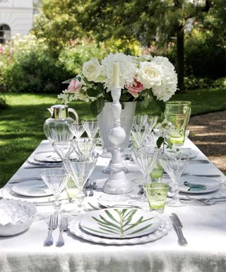 A close-up shot of a dining table outside with a white table cloth and green and white crockery