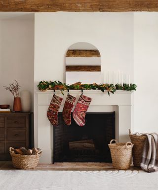 Decorative Christmas stockings hanging from mantel with foliage, wicker basket and blankets surrounding