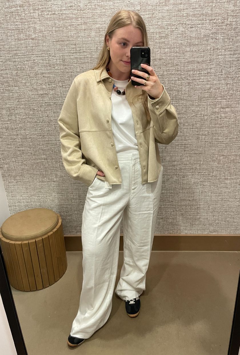 Woman wears suede jacket, white T-shirt, white linen trousers, black trainers