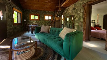 A green velvet couch and wicker table in a stone building surrounded by wooden walls and a wooden staircase built by Charlie Chaplin at Huttopia in California