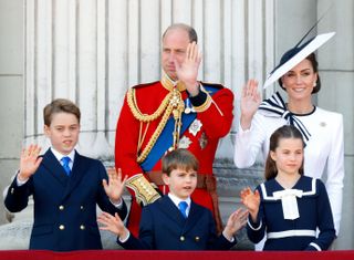 Prince George, Prince Louis, Princess Charlotte, Prince William and Kate Middleton wearing dress clothes and waving on the Buckingham Palace balcony