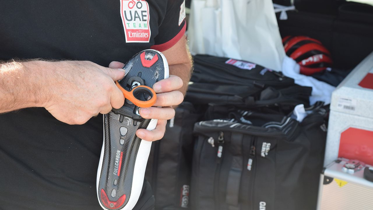 A team mechanic removes the wire mesh from a rider's shoe to improve ventilation in the hot Australian summer