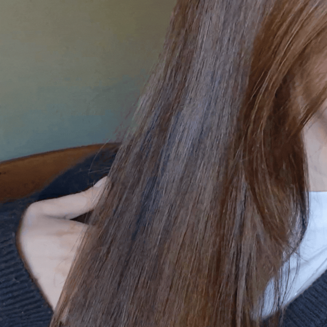 A GIF/video showing a close-up of a strand of Digital Beauty Writer, Naomi Jamieson's hair with the Aveda Miraculous oil applied, being moved up and down to show its reflective shine.