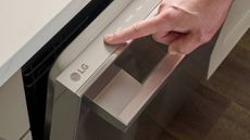 A person's hand switching on an LG dishwasher.