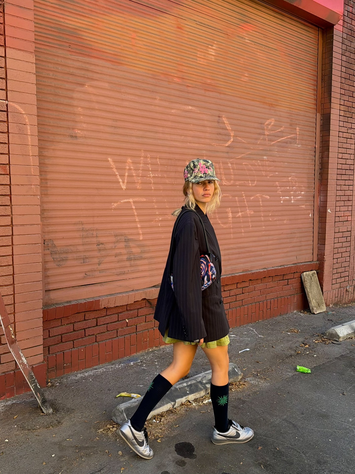 Fashion person Tori van Breugel, @torivanbreugel wears a leather trainer outfit 2026. She wears metallic trainers a pleated mini skirt and over sized blazer.