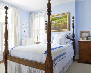 A blue bedroom with wooden four poster bed and white linen