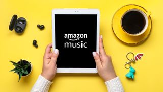 Una mujer sosteniendo una tablet con la aplicación Amazon Music, sobre una mesa amarilla.