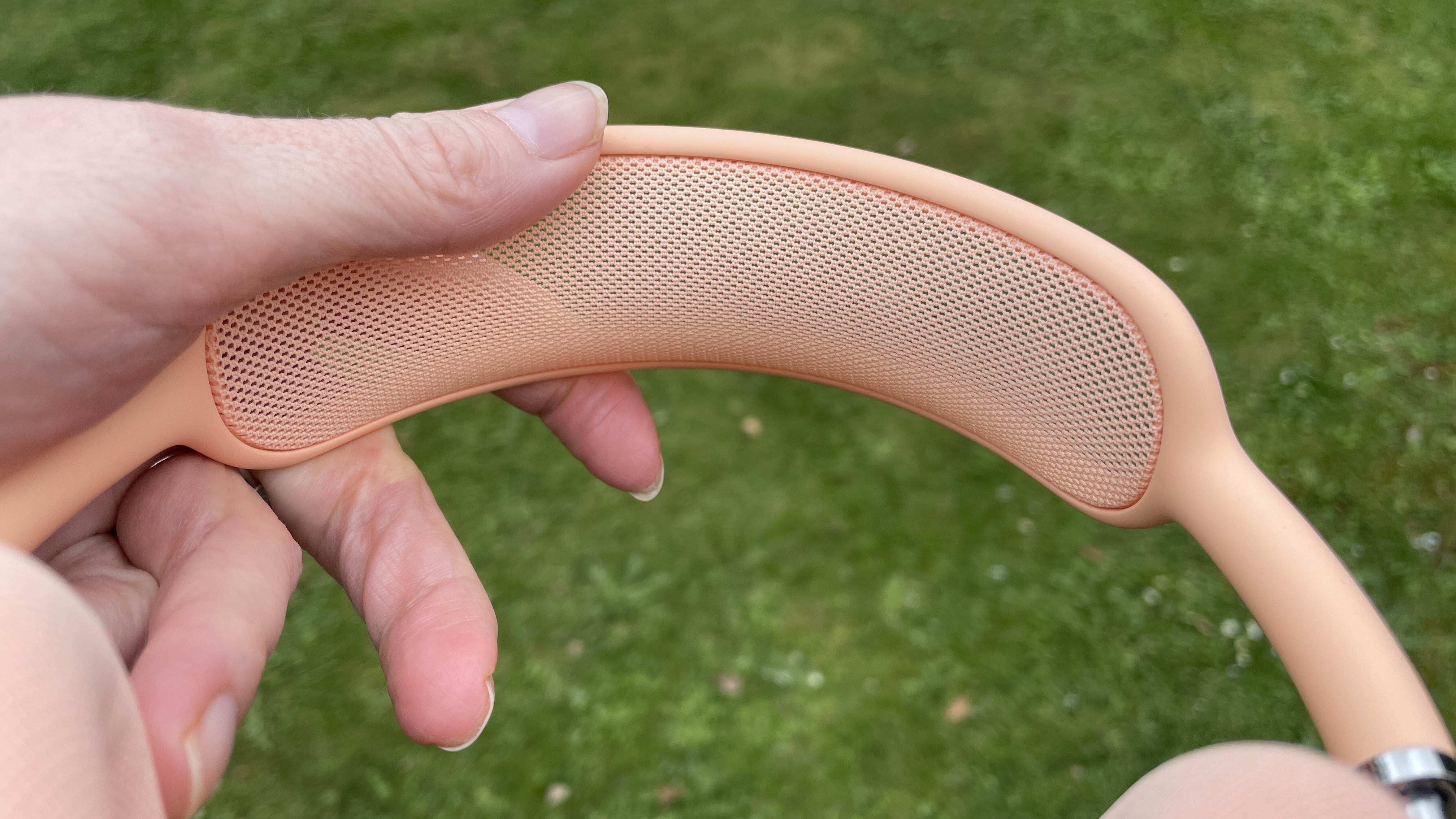 AirPods Max 2 in a garden, held in a hand, in close-up to show the ear cups and band