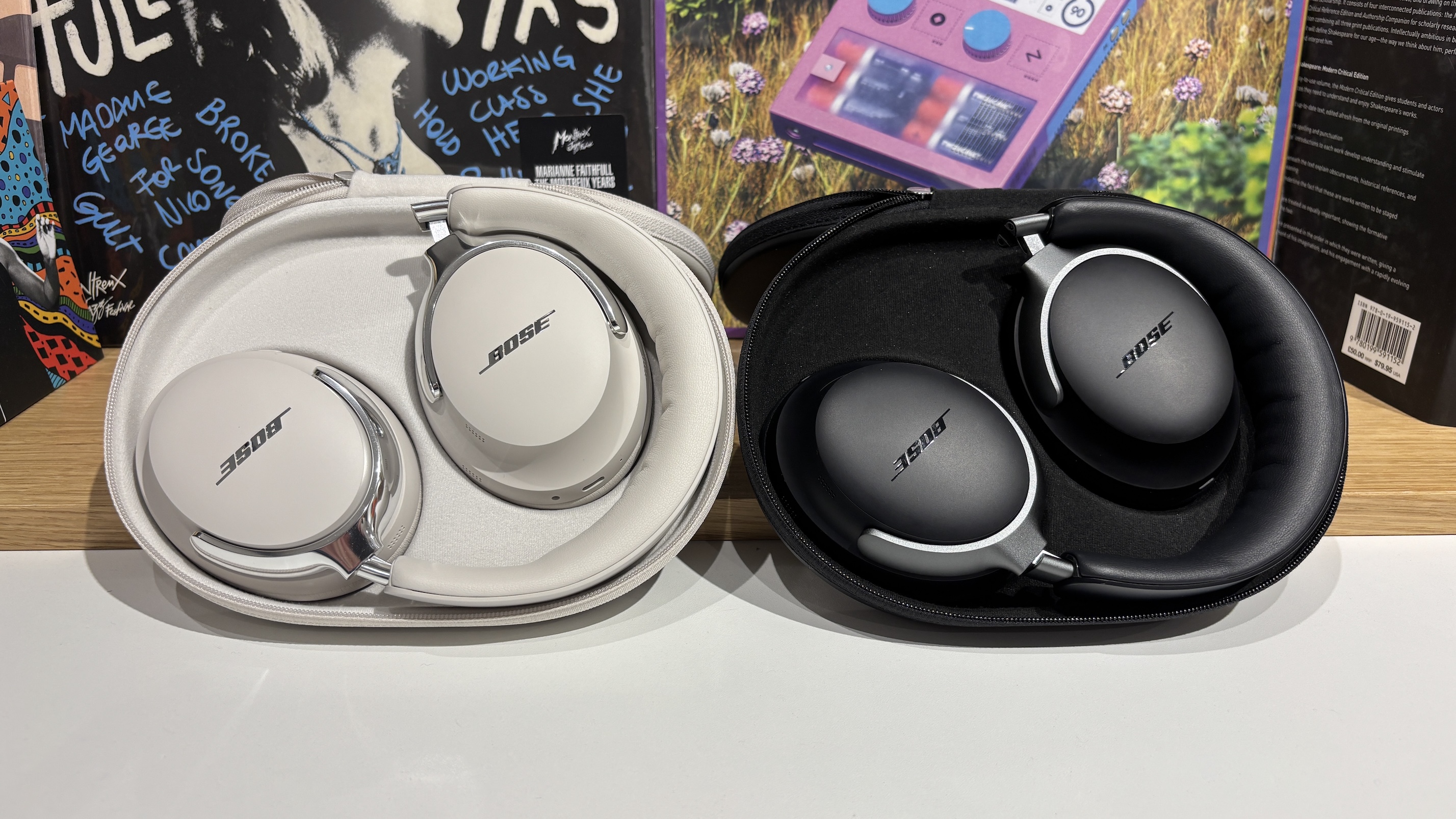 A pair of Bose QuietComfort Ultra Headphones (2nd Gen) and their first-gen predecessors lying balled up in their respective carry cases propped up against a wall.