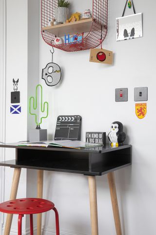 Kid's study area with black and oak desk, red stool, red mesh shelves and cartoon accessories