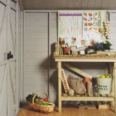 The inside of a light grey shed with a storage bench filled with gardening tools and produce