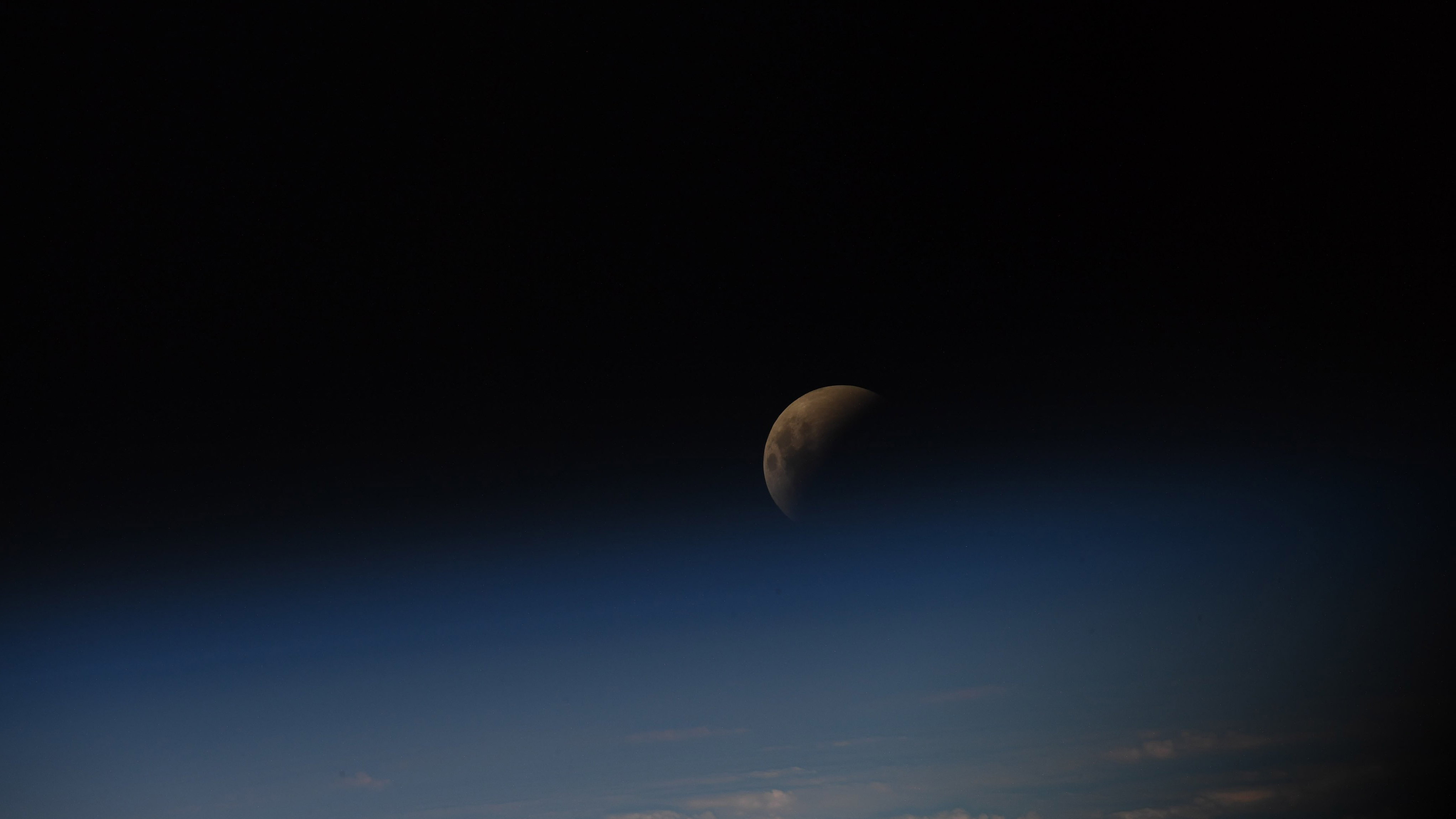 The eclipsed moon peeking through the solar panels of the International Space Station