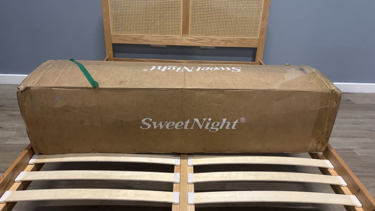 The SweetNight CoolNest Mattress shipping box on a wooden bed frame ready to be opened.