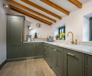 kitchen area with sloped beamed ceiling, green cabinets, small appliances on work top, sink and wooden effect floor