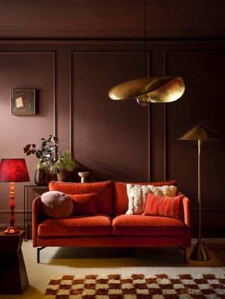 A burgundy living room with a red sofa and gold light fixtures including a pendant shade and a floor lamp