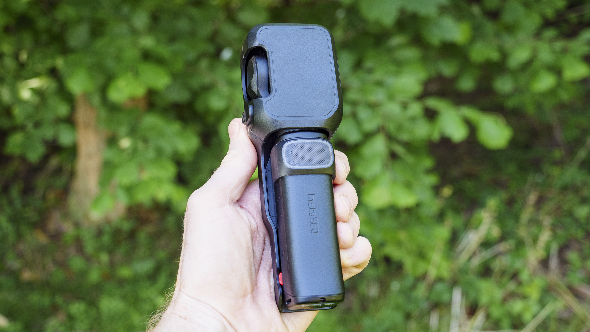 Insta360 Luna Ultra vlogging camera in person's hand, inside its protective case, leafy background