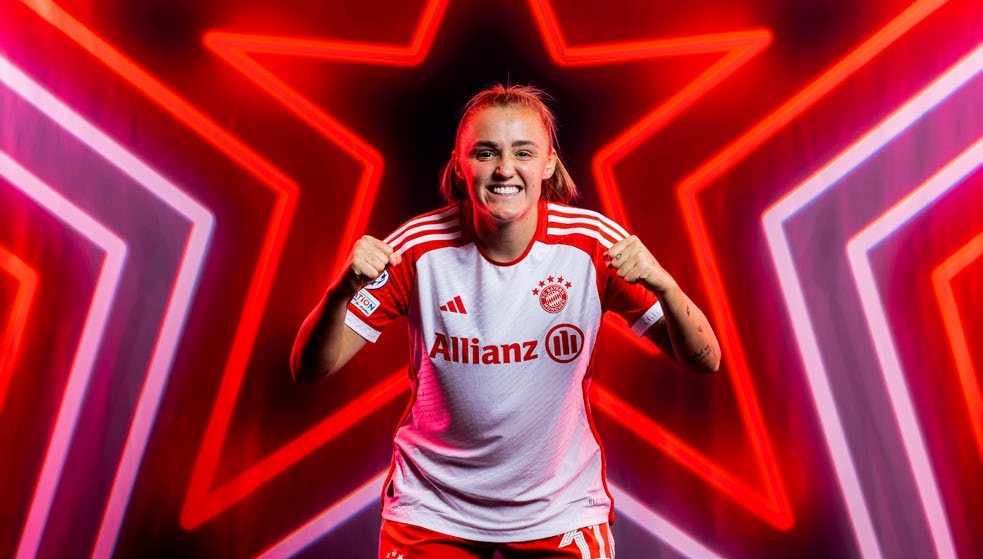 A female football player in a Bayern Munich jersey celebrates with clenched fists against a backdrop of vibrant red and white star lights.