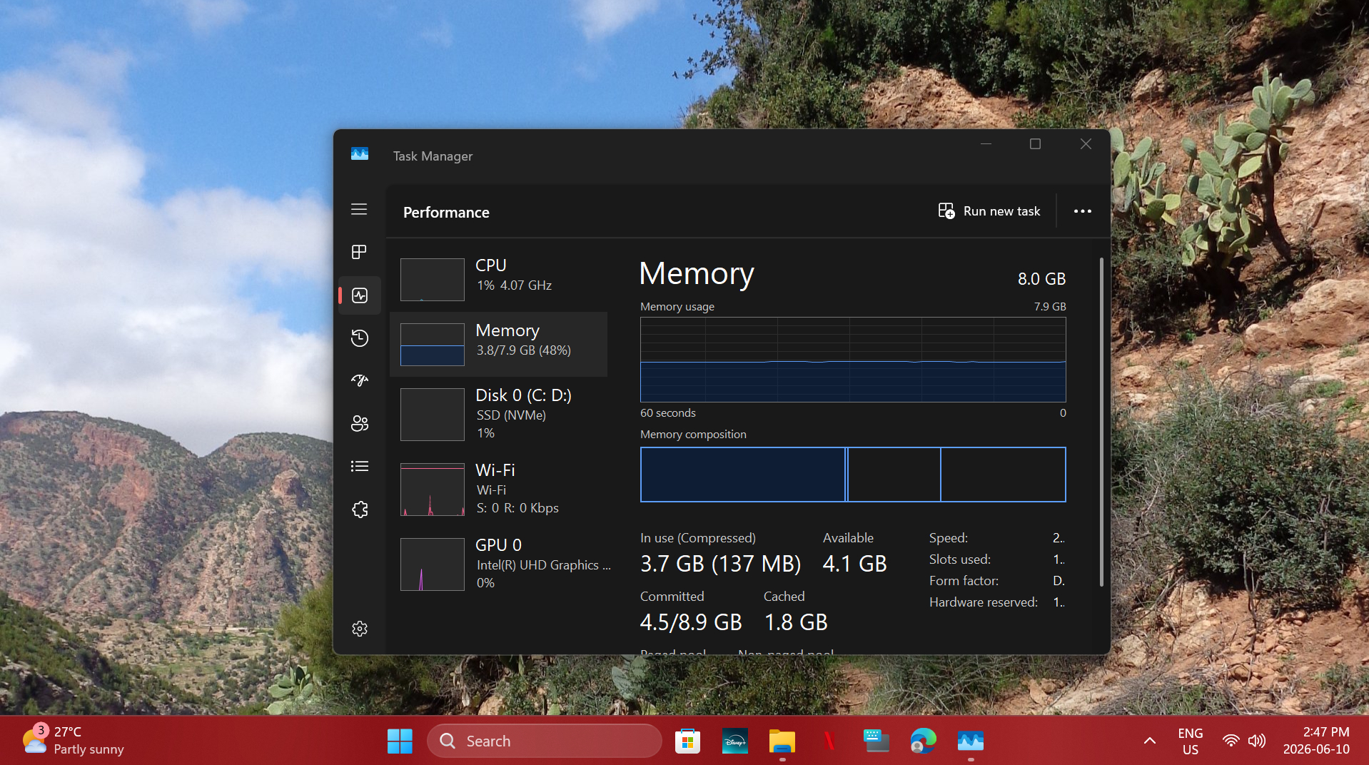 Computer desktop with Windows Task Manager open, showing system performance metrics against a mountain landscape background.
