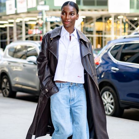 Michaela Coel walks down the street in New York wearing low-rise cuffed jeans with a white shirt, a leather trench coat and Chanel's high-vamp pumps.