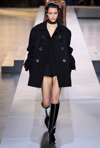 best riding boots shown in a photo from Gucci's fall 2024 runway show with a model wearing a black peacoat with a black top, hot pants, and black riding boots