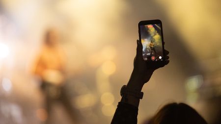 A hand holding a phone aloft at a concert to record an artist