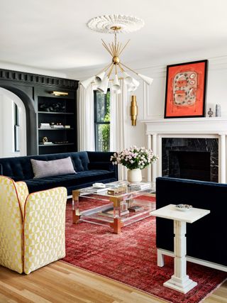 living room with matching midnight blue couches, black bookcase, artwork, red rug, glass coffee table, yellow armchair