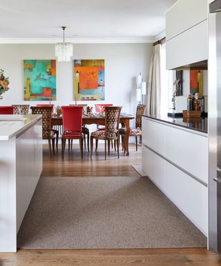 Kitchen wall decor in an open plan space, with bright artwork in a white scheme with red chairs.