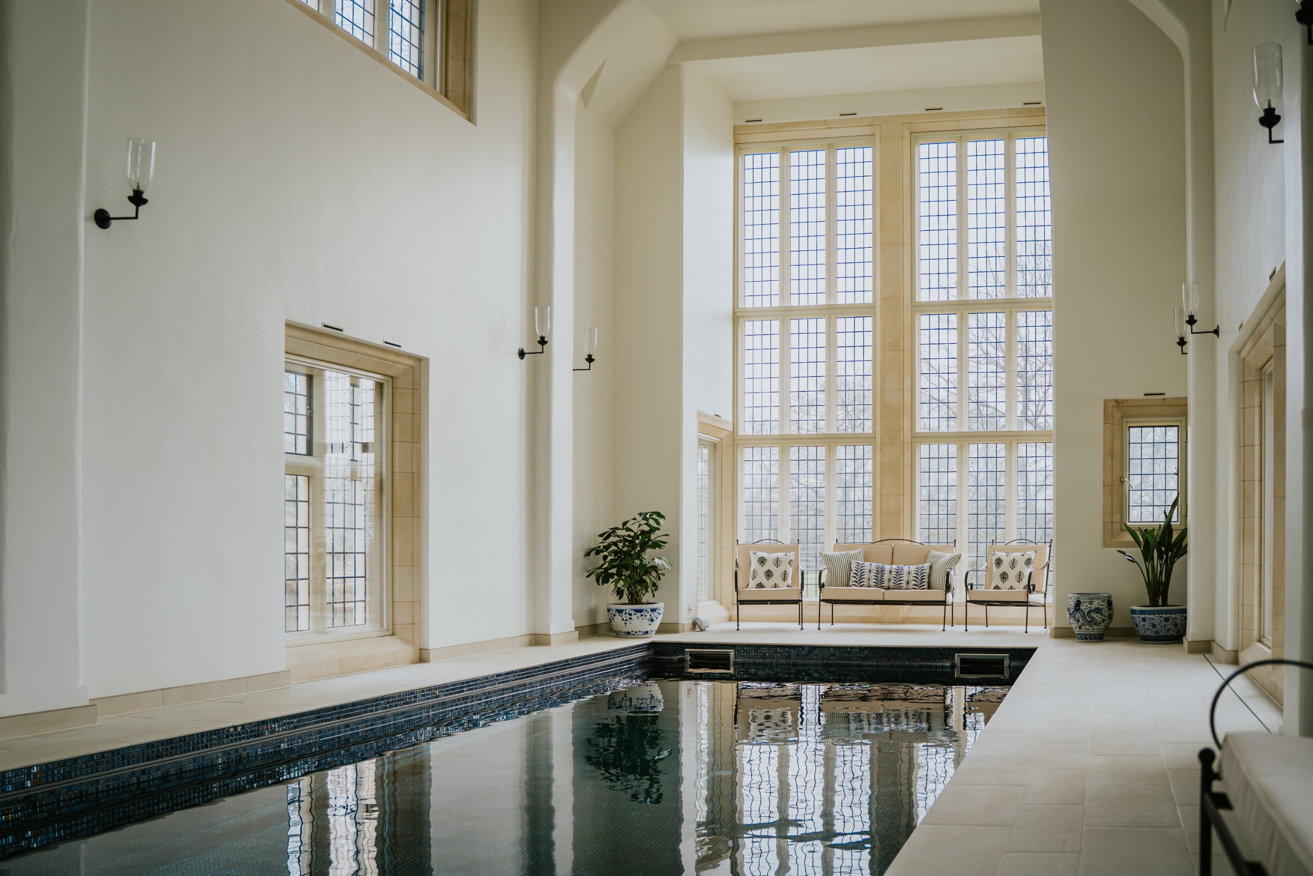 A double-height pool room with creamy walls and mullioned windows