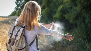 how to avoid tick bites: woman spraying repellent