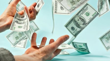 Closeup of 100 dollar bills falling into the hands of a man against a blue background