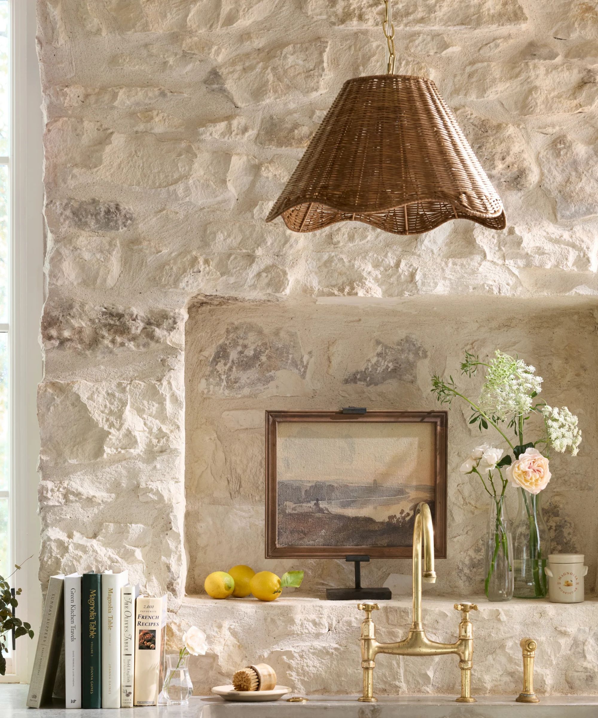 A kitchen with stone walls, brass hardware, and a rattan pendant light