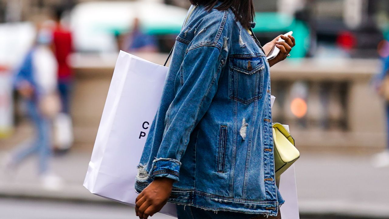 A passerby wears a blue ripped denim jacket, a yellow bag, a large white paper shopping bag, on July 04, 2020 in Paris, France. (Photo by Edward Berthelot/Getty Images)