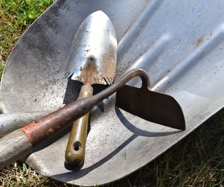 A stainless steel trowel and a carbon steel hoe on a stainless steel shovel