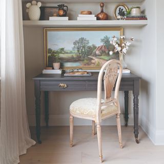 A home office nook with a vintage desk and chair and a painting on top of the desk