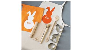 A child's cream apron, orange drawstring bag, rolling pin, wooden spoon, wooden spatula and animal shaped cookie cutters all personalised with the name Erin and a corresponding Easter bunny logo.